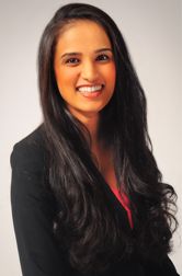 Dr. Megha Patel, MD Smiling with long black hair and a black blazer over a red top. She is posing against a plain background, conveying a professional and cheerful tone.
